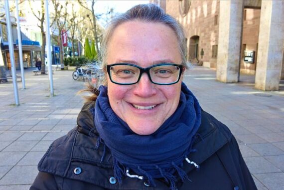 Reisebloggerin Stefanie Armbruster vom Reiseblog Steffistraumzeit steht lächelnd in einer Fußgängerzone mit Winterjacke und dunkelblauem Schal. Im Hintergrund sind Gebäude, Schaufenster und Bäume ohne Laub zu sehen – ein klarer Wintertag in einer Stadt. Das Bild symbolisiert ihre Leidenschaft für Slow Travel, authentische Begegnungen und individuelle Reisen, über die sie auf ihrem Blog berichtet